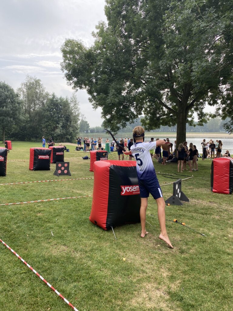scholieren spelen archery tag op een grasveld met opblaasbare obstakels